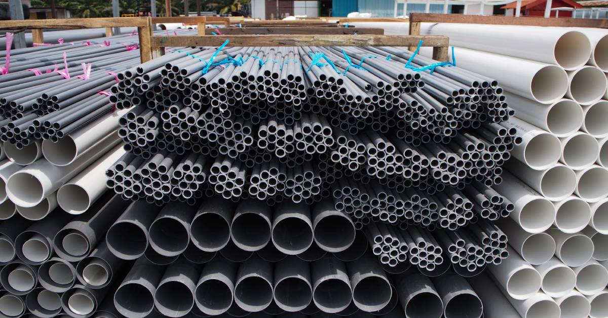 A massive pile of gray and white PVC pipes stacked within a wooden frame. The PVC pipes vary wildly in size.