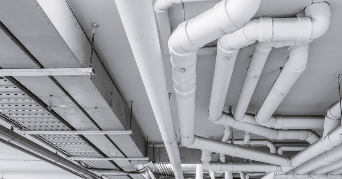 A huge PVC pipe system is installed on the ceiling. The pipes are installed next to a large ventilation system.