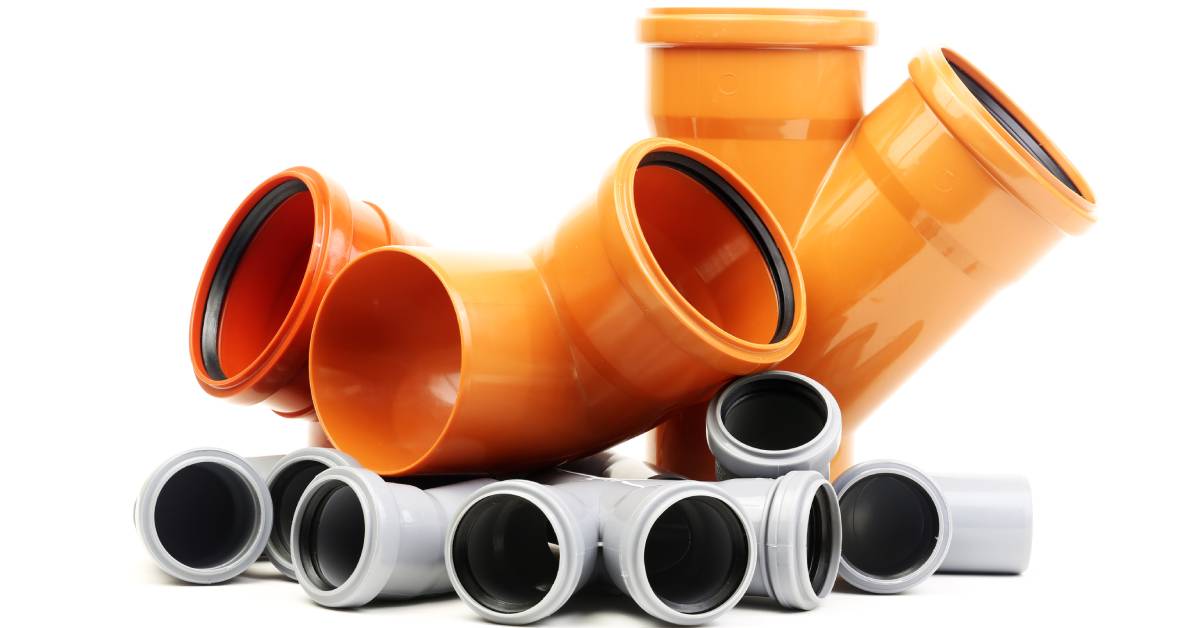 Three large pieces of a PVC plumbing system are sitting on a short pile of smaller PVC pipe components.