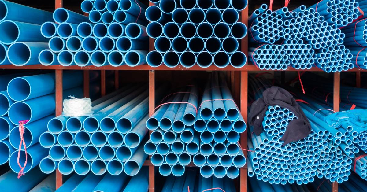 Many blue PVC pipes are bundled together with thin orange materials. The bundles are sitting on large orange shelves.