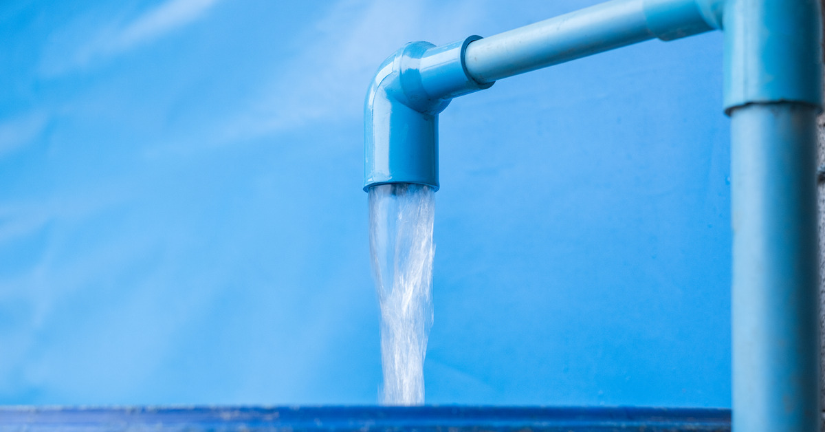 Water is draining out of bright blue PVC pipes. The water is going into a blue bucket below the PVC.