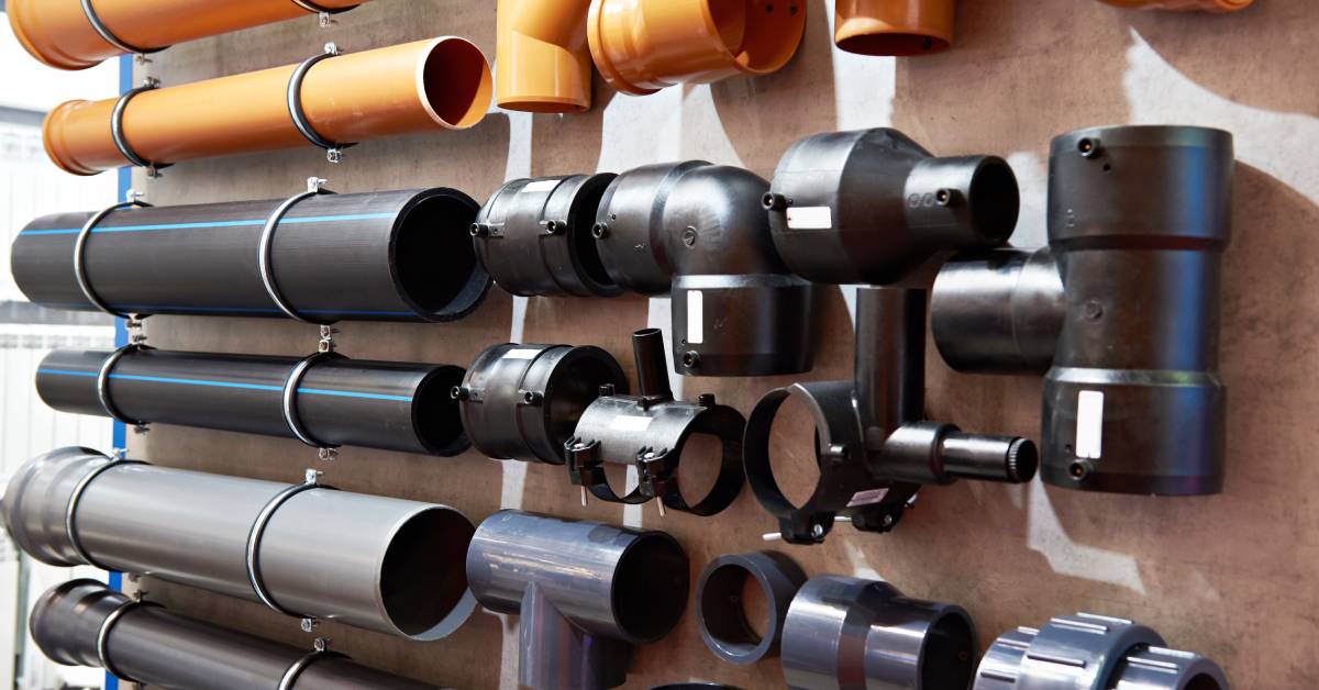 A group of orange, black, and gray PVC pipe fittings are hanging on a wall. Bright sunlight is shining on the fittings.