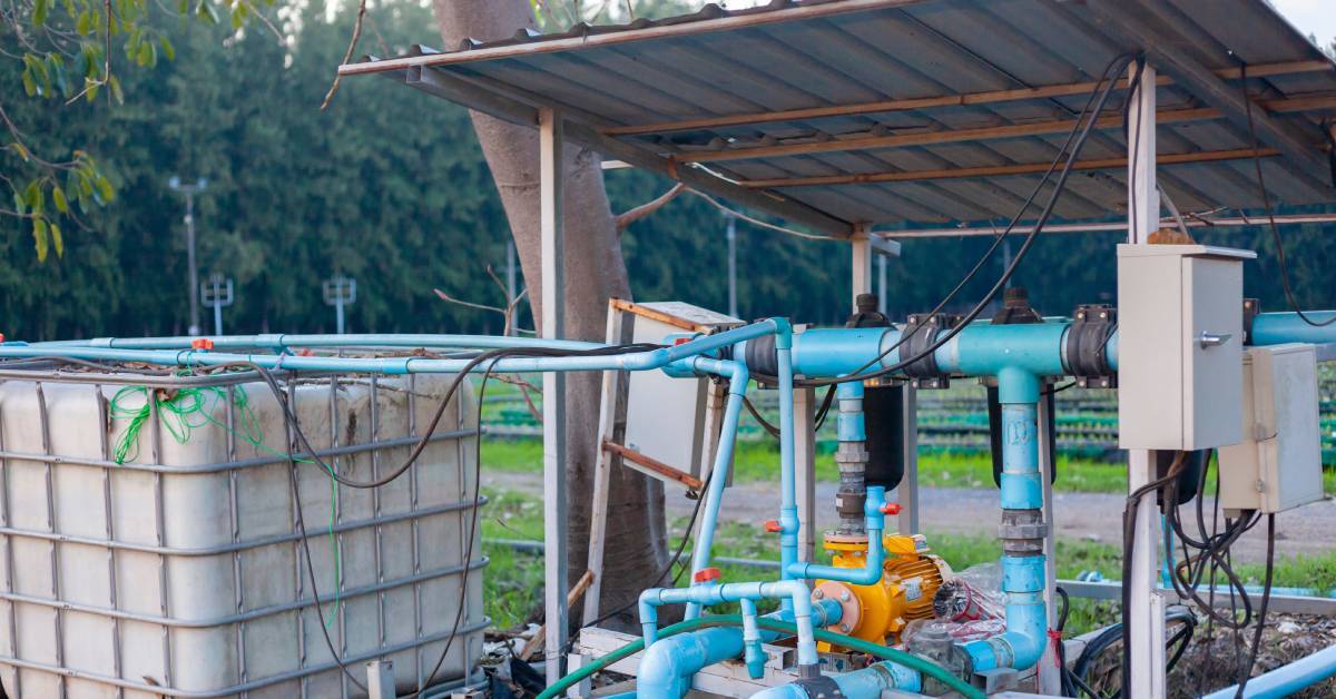 An outdoor plumbing system on a farm surrounded by green trees. The system is comprised of blue PVC pipes.